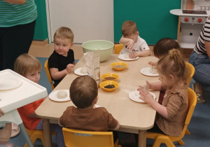 dzieci siedzą przy stoliku i ugniatają ciasto