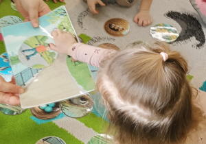 dzieci siedzą na dywanie, dziewczynka podaje wybrany obrazek