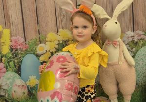 dziewczynka uśmiecha się, trzyma balona pisankę i ma na głowie opaskę uszy królika