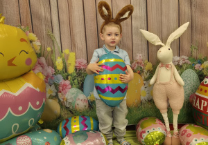 chłopiec z opaską na głowie uszy królika, uśmiecha się i trzyma balona pisankę