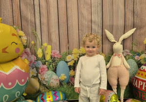 chłopiec stoi , wokół niego leżą balony pisanki, uśmiecha się