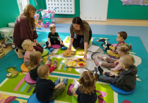 dzieci i opiekunki siedzą na dywanie, słuchają czytanego opowiadania