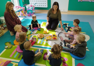 dzieci i opiekunki siedzą na dywanie, mówią co ciocia przyniosła na tacy