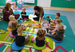 dzieci i opiekunki siedzą na dywanie, słuchają opowiadania i patrzą jak powstaje gofrowy zajączek