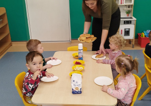 opiekunka rozdaje dzieciom siedzącym przy stoliku gofry