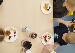 dzieci siedzą przy stolikach przed nimi leżą ozdobione gofry