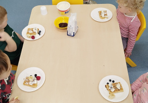 dzieci siedzą przy stoliku przed nimi leżą ozdobione gofry