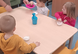 dzieci siedzą przy stoliku i sypią ziarenka do kubeczków