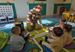 dzieci siedzą na dywanie , opiekunka pokazuje palemkę
