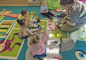 opiekunka pokazuje dzieciom siedzącym na dywanie co znajduje się w koszyczku