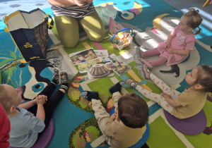 dzieci siedzą na dywanie, a przed nimi leżą zdjęcia wielkanocnych symboli