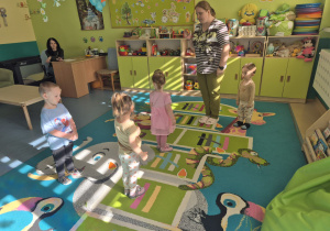 dzieci i opiekunka stoją na dywanie- zabawa ruchowa