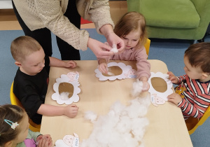 dzieci przy stoliku wyklejają baranki i opiekunka pomaga