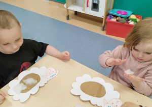 chłopiec patrzy, przed nim leży baranek, a dziewczynka ugniata watę