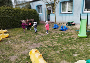 opiekunka trzyma wiaderko, dzieci noszą jajka na łyżkach