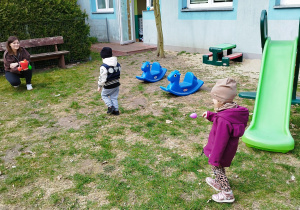 opiekunka trzyma wiaderko, dzieci noszą jajka na łyżkach