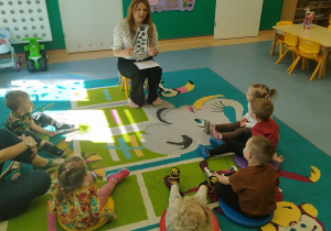 dzieci siedzą na dywanie, opiekunka pokazuje im pingwina