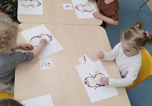 dzieci siedzą przy stolikach, wyklejają pingwiny kulkami plasteliny