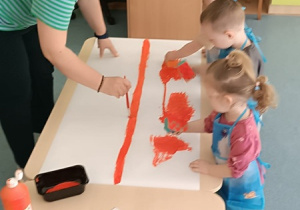 opiekunka maluje kreskę na kartonie pędzelkiem, a dzieci rozprowadzają farbę gąbkami