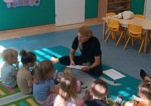 dzieci i pani pedagog siedzą na dywanie, słuchają czytanej bajki