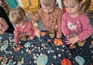 dzieci przy użyciu pęset zbierają kamyki