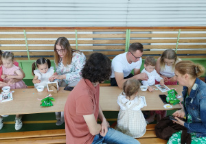 rodzice wraz z dziećmi siedzą przy stolikach i przyklejają naklejki