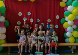 dzieci siedzą na ławce i stoją a przed nimi leżą prezenty ufundowane przez rodziców