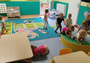 dzieci chodzą jedno za drugim pokonując przeszkodę, przechodząc pod stolikiem i depcząc płytki sensoryczne