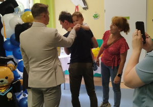chłopiec trzymany przez tatę podaje rękę panu burmistrzowi, mama stoi i sie uśmiecha