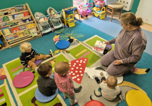 dzieci wraz z opiekunką na dywanie, przed nimi leży papierowy muchomor