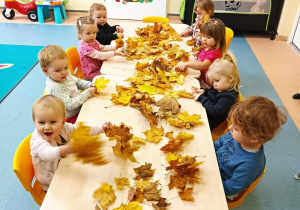 dzieci siedzą przy stoliku, a na nim rozsypane liście